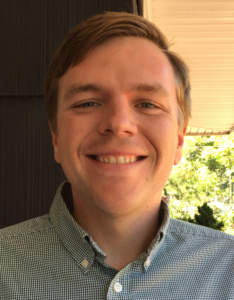 smiling man, with short hair parted to the side, wearing a button down shirt
