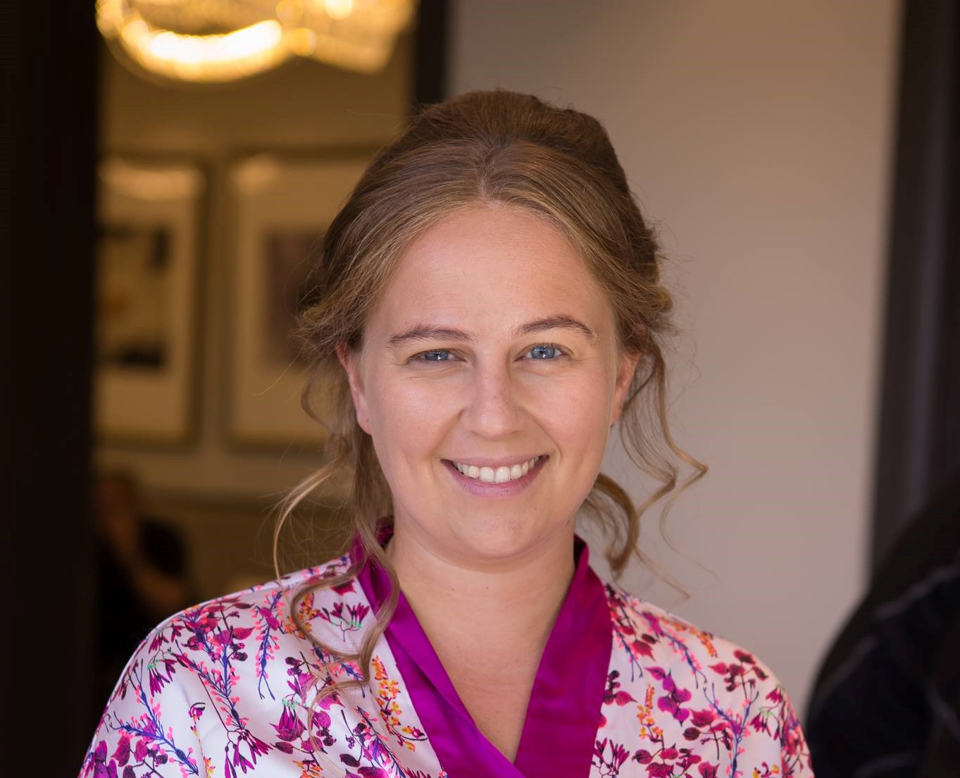 shely esses head shot. smiling female with medium length blonde hair, wearing a flowery white and purple shirt.